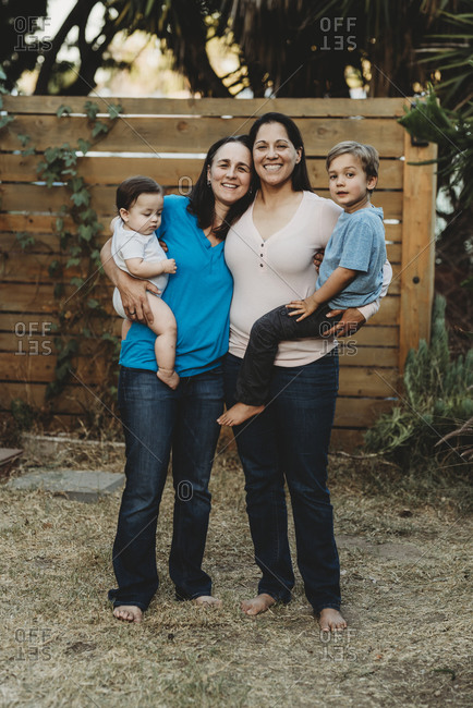 Smiling moms holding their baby and 5 yr old son outdoors near fence