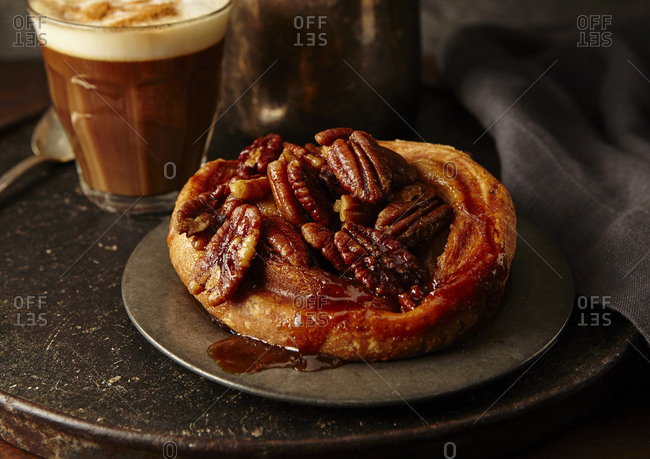 Cinnamon pecan roll in moody setting with cappuccino