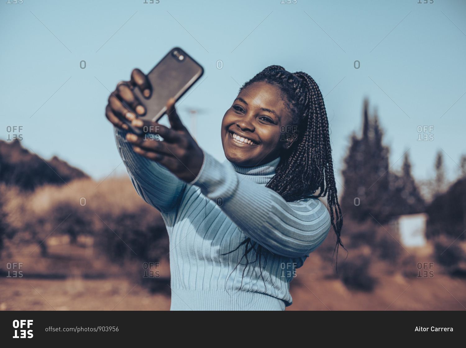 Smiling young woman with braids taking selfies in a rural setting