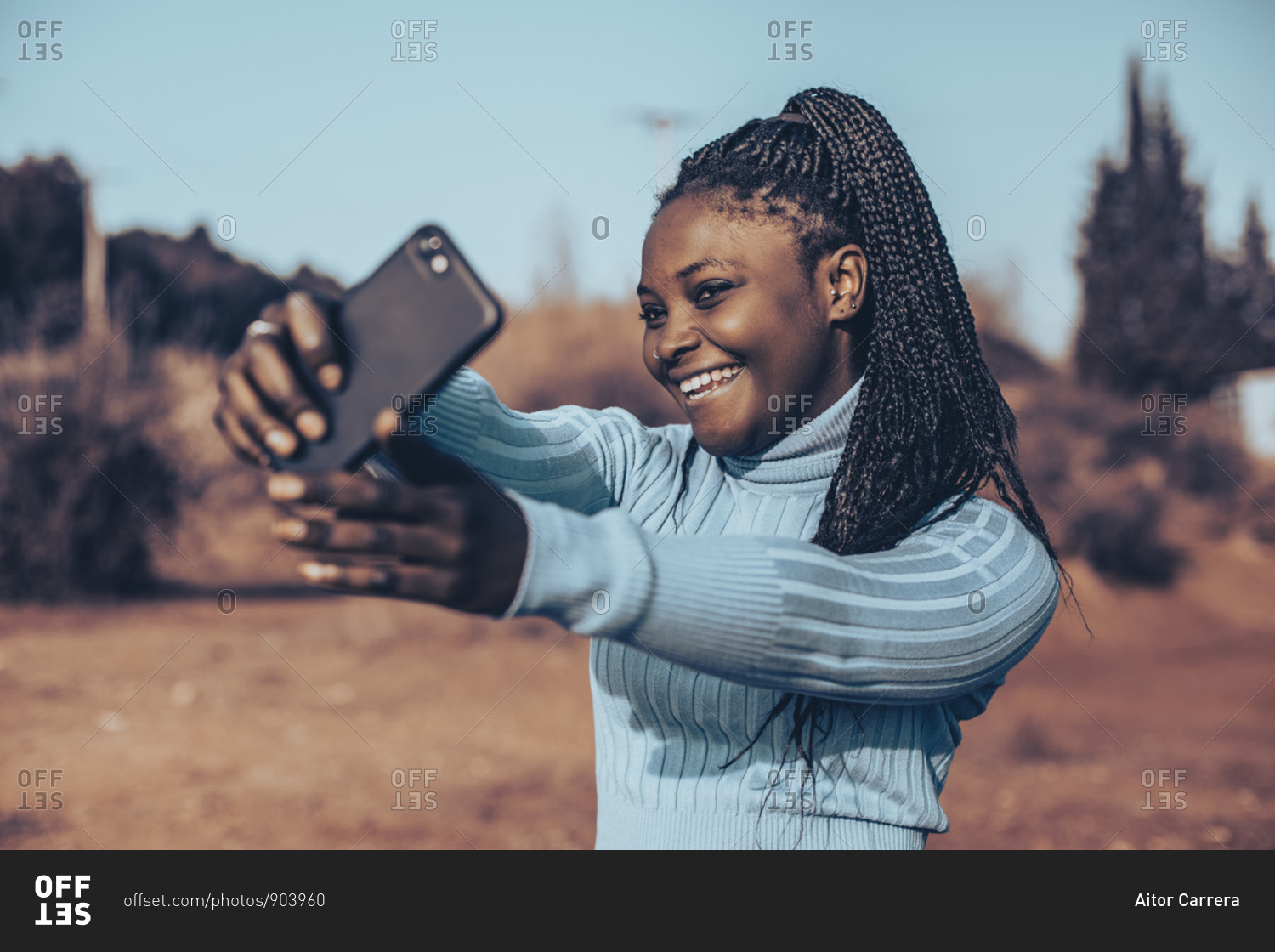Beautiful young woman with braids smiling and taking selfies in a rural setting