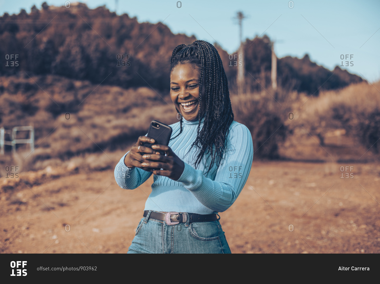 Young woman with braids smiling using cell phone in a rural setting
