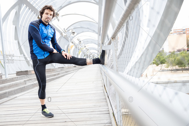 Side view of mature jogger standing on boardwalk and performing basic stretching exercises on bar at river bank at daytime