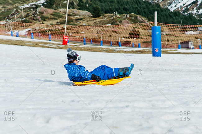 Little child wearing snowboard goggles and winter sport clothes holding onto and riding on sledge in snowy mountains in Candanchu, Huesca, Spain