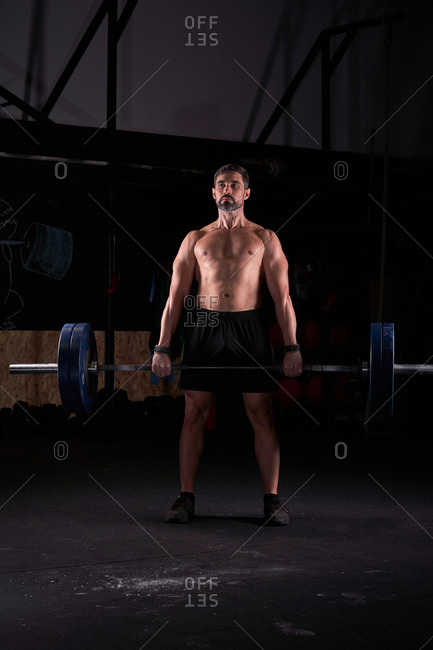 Strong man with barbell with weights in his hands doing strength exercises in the gym with magnesium in his hands. Young athlete practicing multidisciplinary training
