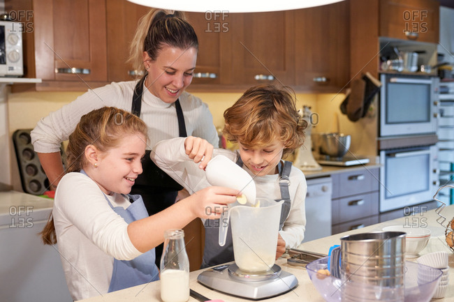 Stock photo of children with a woman wearing an apron in a kitchen preparing cupcake and putting the flour in a meter
