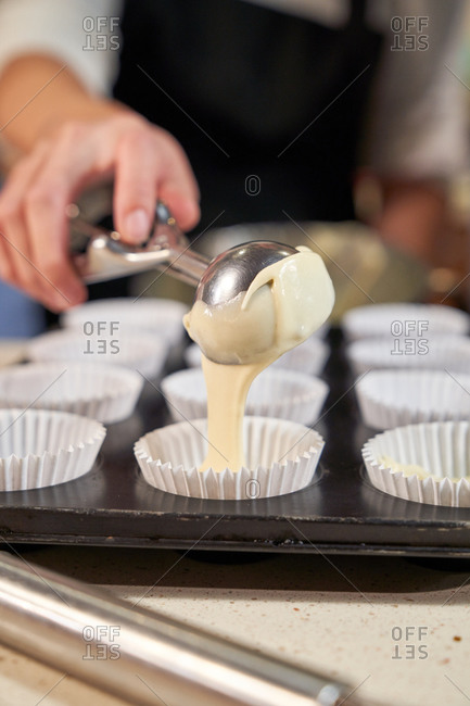 Stock vertical photo of a detail of a hand emptying cream with the ice cream scoops in plates prepared with pastry paper for cupcakes