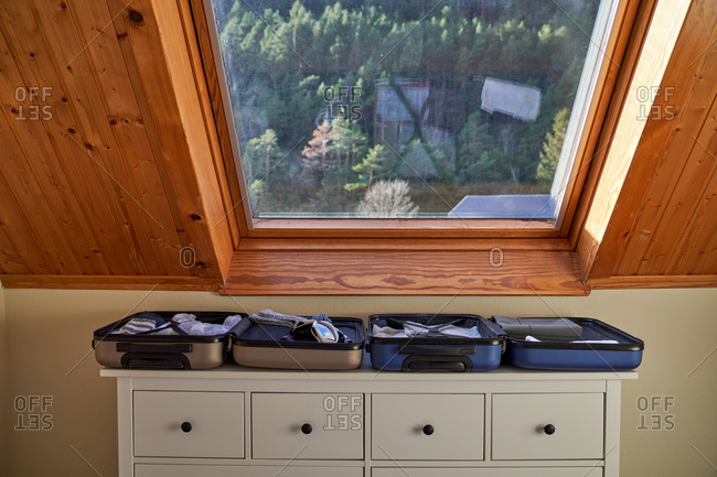 Ski goggles and hat placed in open luggage on top of drawer under window during winter vacation preparation at home