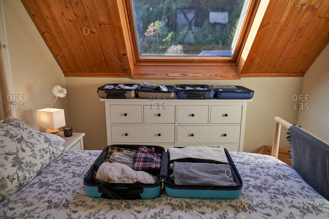 Open luggage with folded clothes placed on bed and dresser in cozy bedroom during journey preparation