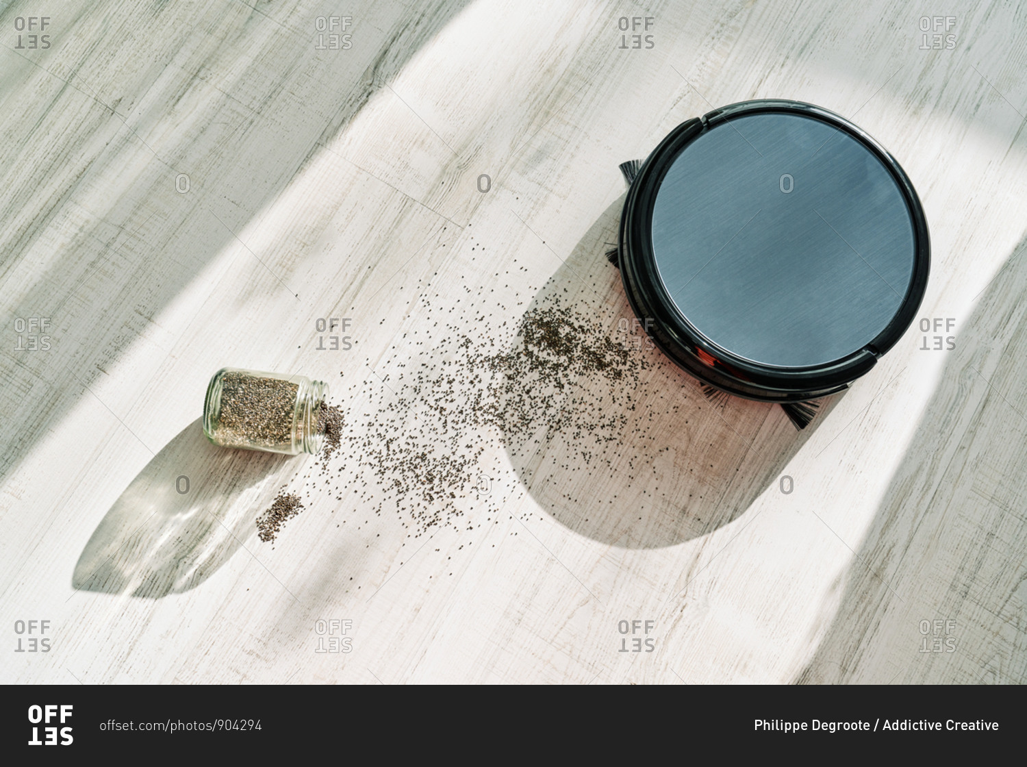 From above of round robotic vacuum cleaner sliding on light laminate floor and removing dirt spilled out of glass pot