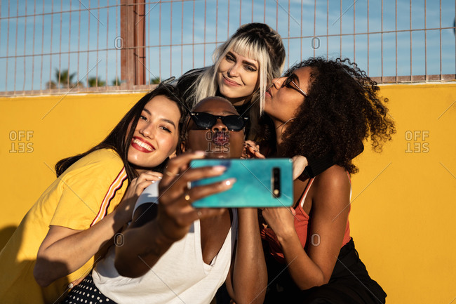 Carefree youthful multiracial women in casual clothes enjoying freedom and taking selfie on cellphone while spending time on stadium