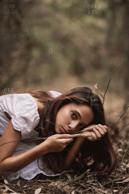Sensual mysterious female in white dress sitting on knees hiding in autumnal foliage looking at camera