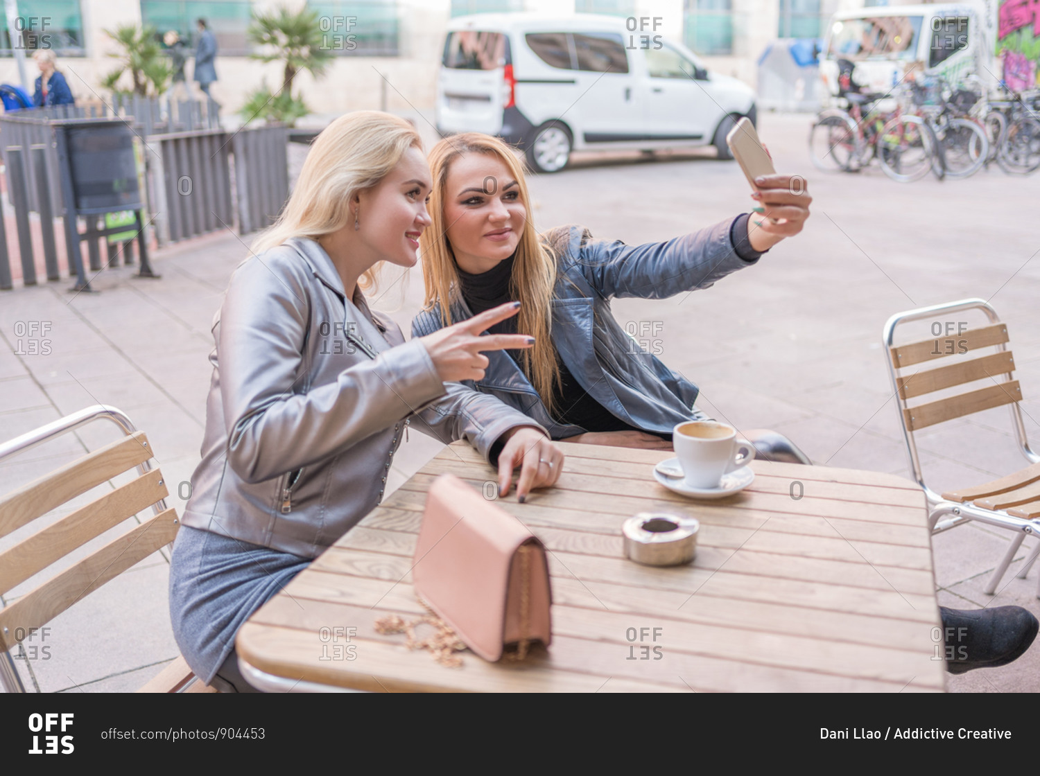 From above of content stylish ladies in casual clothing taking selfie on mobile phone while drinking coffee on outdoors terrace of cafe