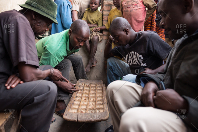 Ruanda, Africa - December 14, 2019: Group of focused African men playing board game sitting on street in village