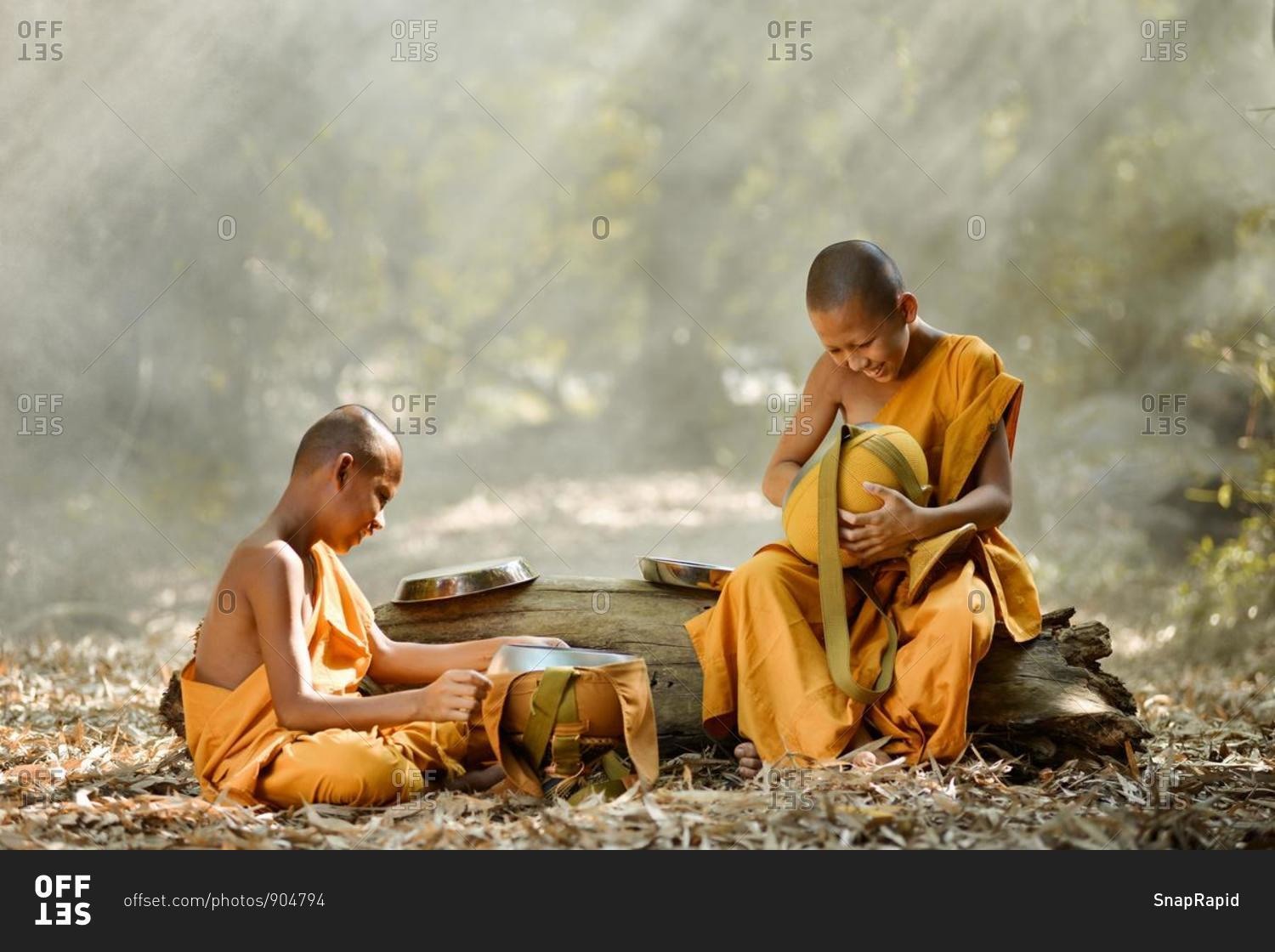 two-novice-buddhist-monks-sitting-in-forest-cleaning-food-bowls