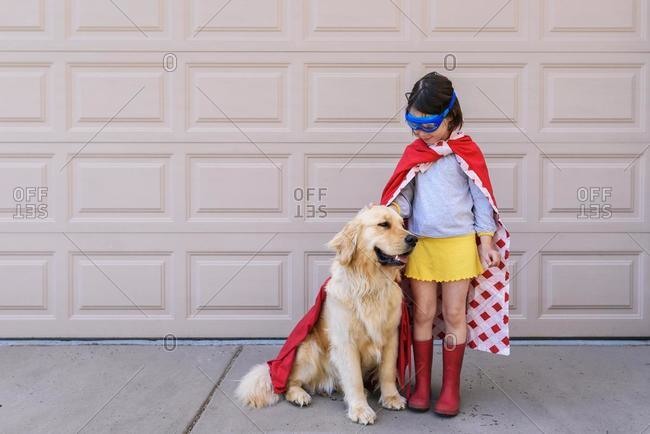Girl dressed as a superhero standing by the garage with her golden retriever dog