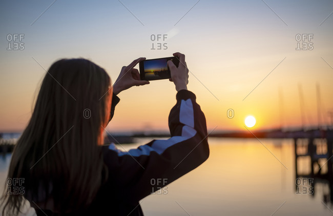 Germany- Mecklenburg-West Pomerania- Poel Island- Rear view of teenage girl photographing sea at sunset