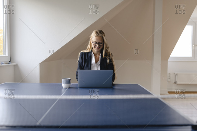 Young businesswoman using laptop on table tennis table in office