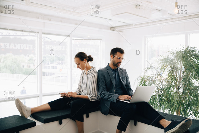 Male and female colleagues using technologies while sitting at corridor in creative office