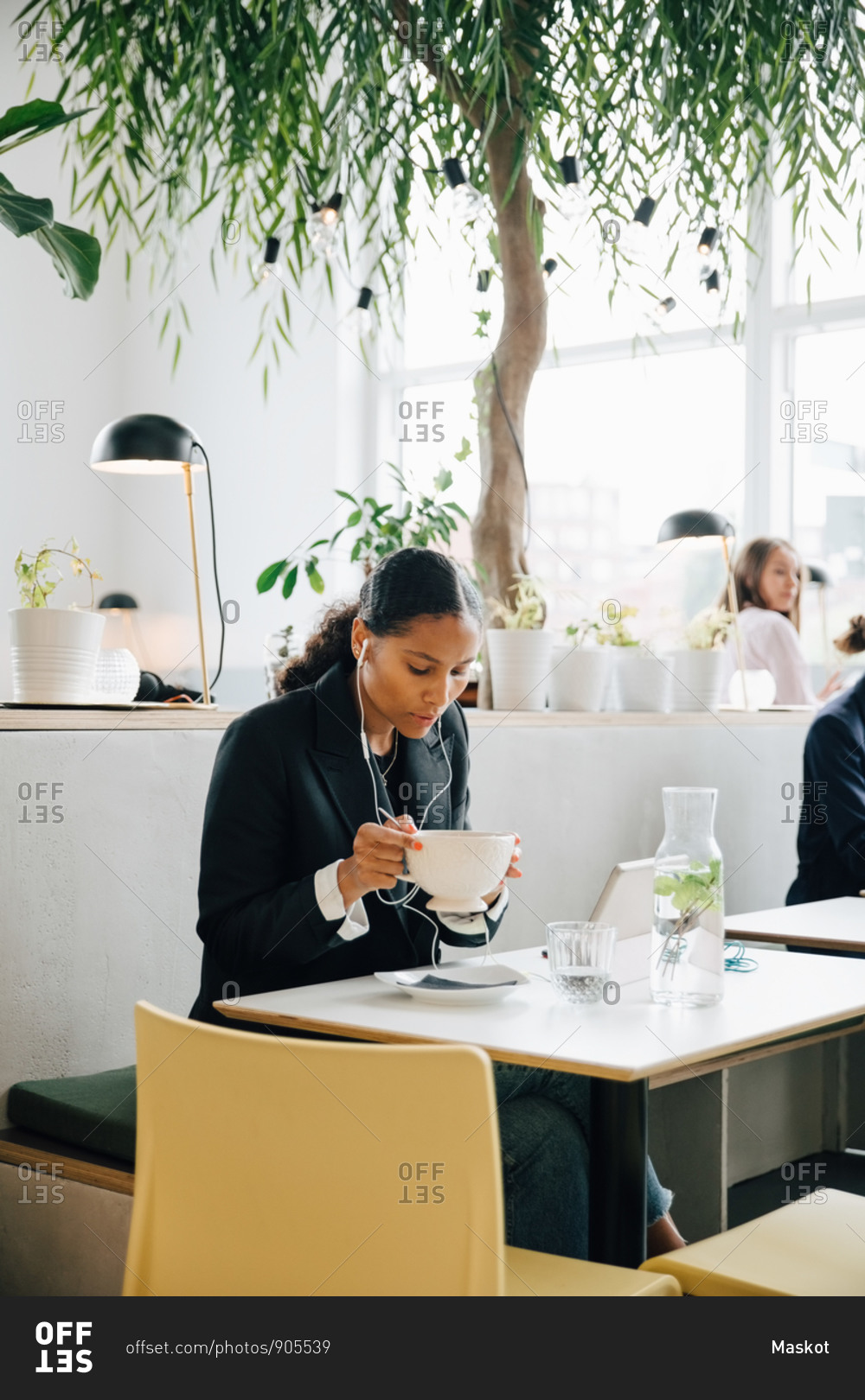 Businesswoman wearing headphones having soup at office cafe