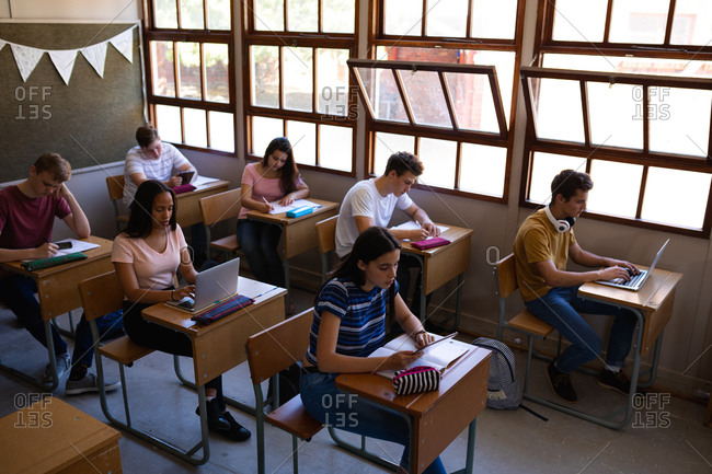 High angle view of a multi-ethnic group of teenage concentrating pupils sitting at desks in class studying at school in a high school