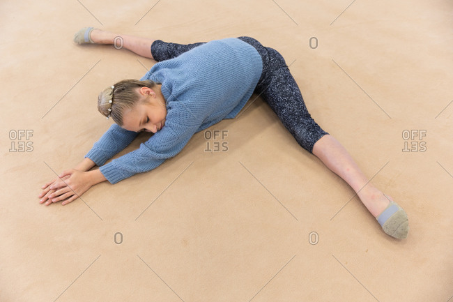 High angle side view of teenage Caucasian female gymnast practicing at the gym, stretching and warming up. Gymnasts training hard for competition.