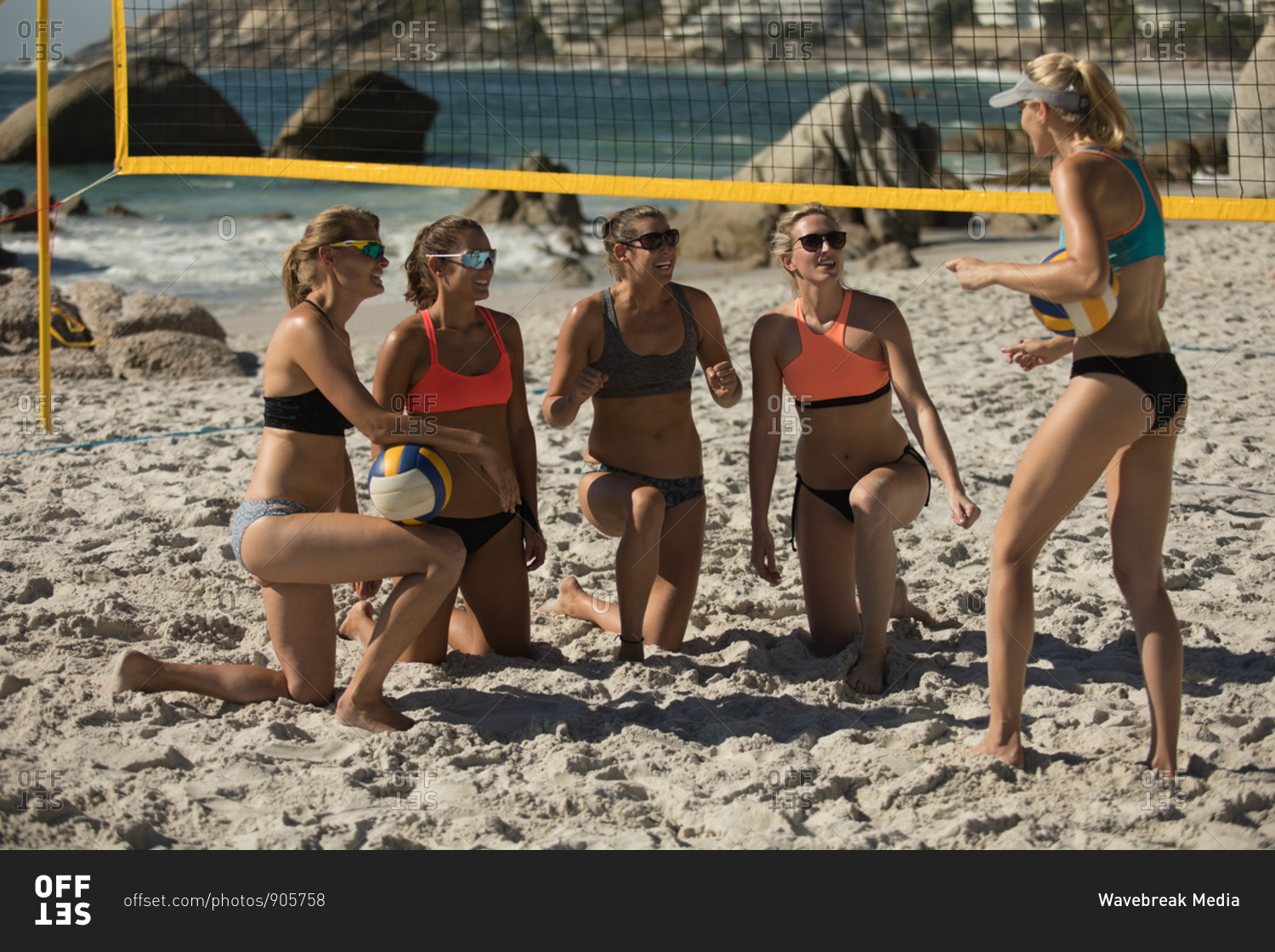 Front view of a group of Caucasian female friends enjoying free time on a beach on a sunny day, two of them holding a ball, one standing and talking