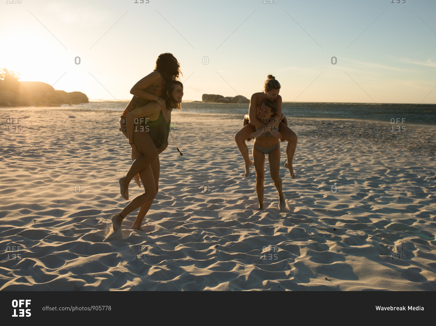 Front view of a group of Caucasian female friends enjoying free time on a beach on a sunny day, carrying each other piggyback