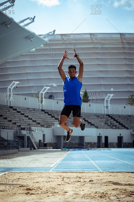 Front view of a mixed race male athlete practicing at a sports stadium, doing a long jump. Track and Field Sports Training in Stadium.