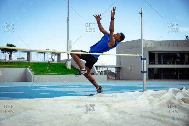 Side view of a mixed race male athlete practicing at a sports stadium, doing a high jump. Track and Field Sports Training in Stadium.
