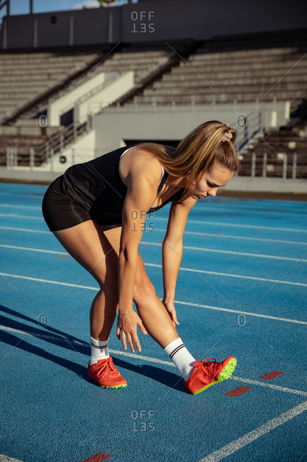 Side view of a Caucasian female athlete practicing at a sports stadium, stretching on a running track. Track and Field Sports Training in Stadium.