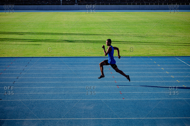 Side view of a mixed race male athlete practicing at a sports stadium, sprinting. Track and Field Sports Training in Stadium.