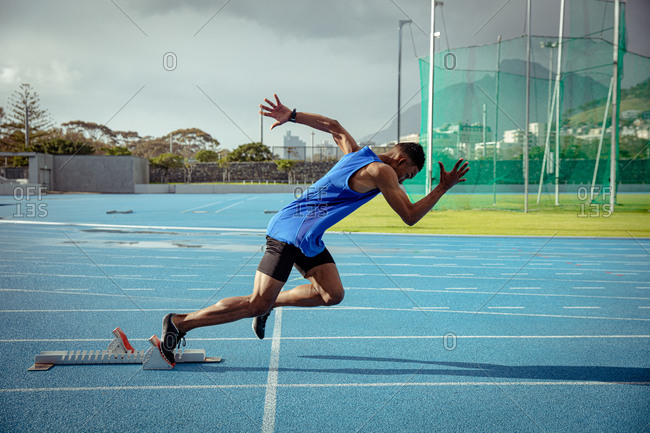Side view of a mixed race male athlete practicing at a sports stadium, starting the race from starting blocks. Track and Field Sports Training in Stadium.