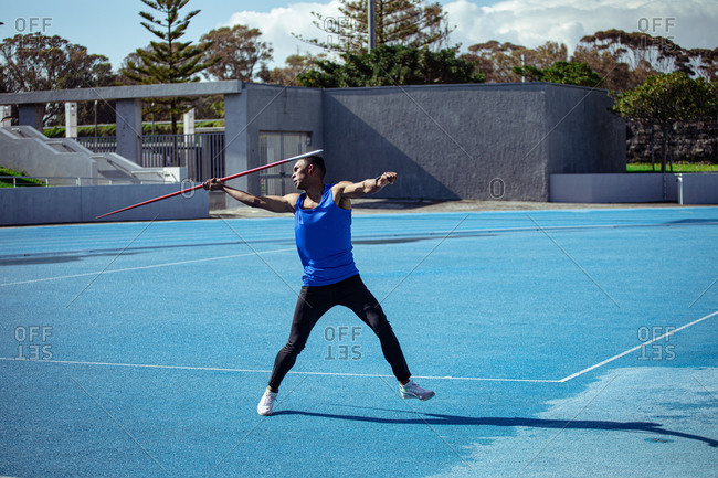 Side view of a mixed race male athlete practicing at a sports stadium, preparing to throw a javelin. Track and Field Sports Training in Stadium.