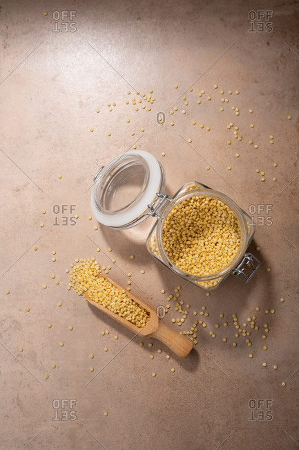 Overhead view of pasta ptitim on light surface with wooden scoop