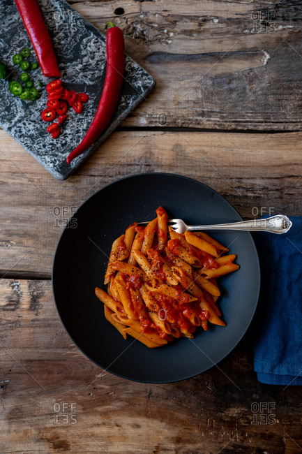 Top view of penne pasta dish with peppers on wooden surface