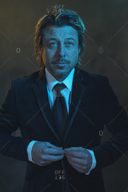 Portrait of a man buttoning his tuxedo under blue light