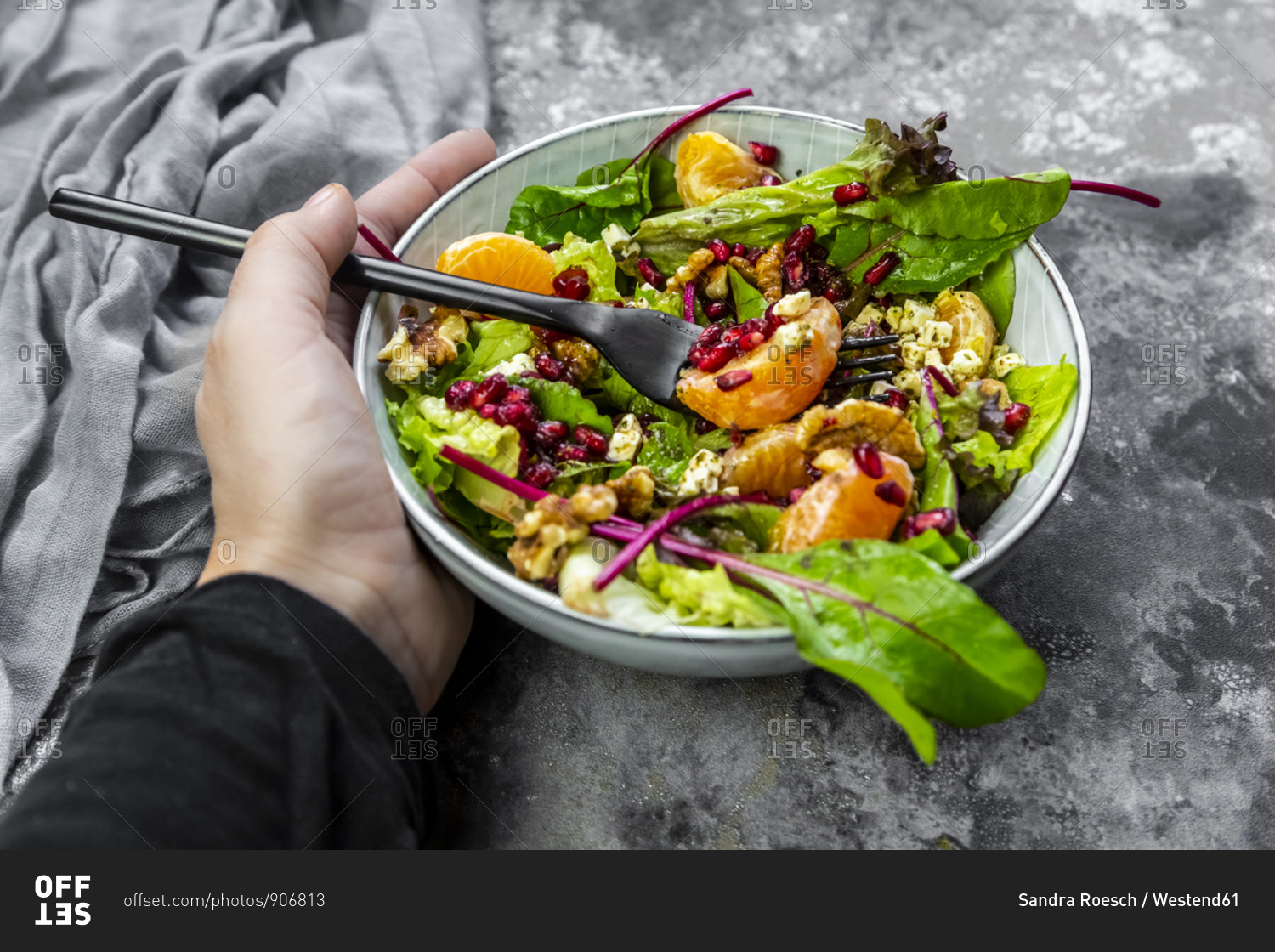 Hand holding bowl of winter salad with lettuce- tangerines- walnuts- feta and pomegranate seeds