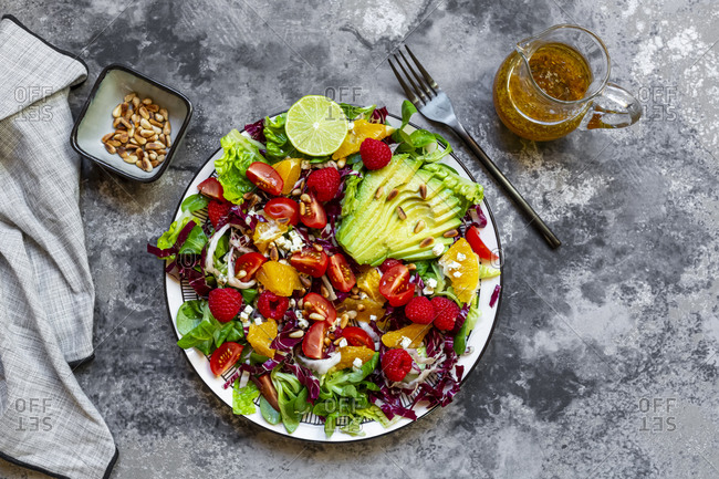 Studio shot of fruity salad plate with lambs lettuce- radicchio- lettuce hearts- avocado- tomato- pine nuts- raspberries- oranges- lime