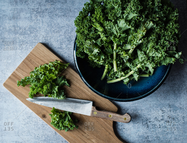 Top view of bowl of kale, cutting board with knife and chopped kale.