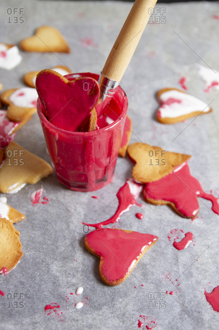 Glass full of red cream to paint biscuits with brush and fallen biscuits