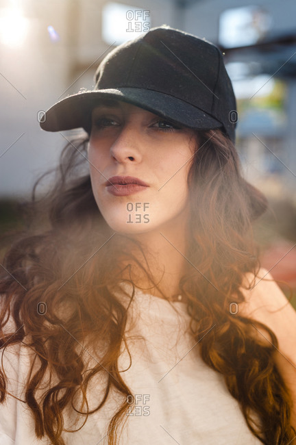 Serious curly woman wearing a cap in the street with lens flare