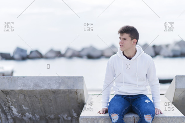 Front view of a teenager wearing casual attire while sitting on a bench outdoors and looking away