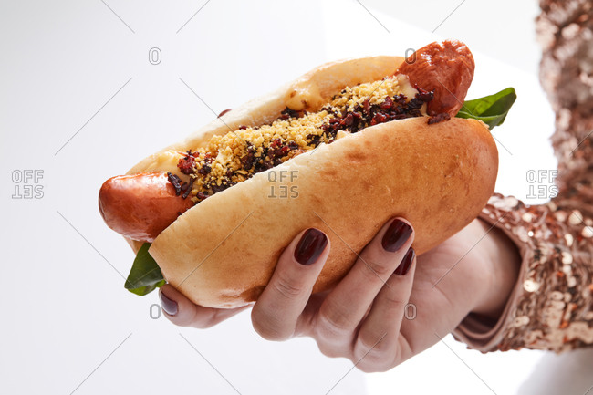 Cropped anonymous person hands with beautiful manicure holding a hot dog on isolated on white background