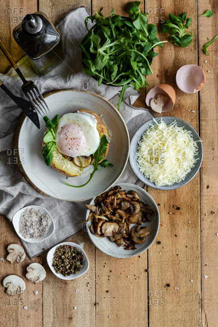Top view fried egg on potato on wooden table with fried mushrooms grated cheese and herbs