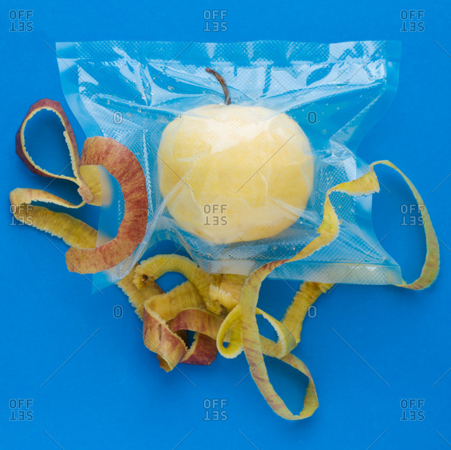 Top view of ripe yellow peeled apple in vacuum plastic bag and apple peel on blue background