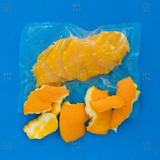 Top view of ripe peeled orange in vacuum plastic bag and orange peel on blue background