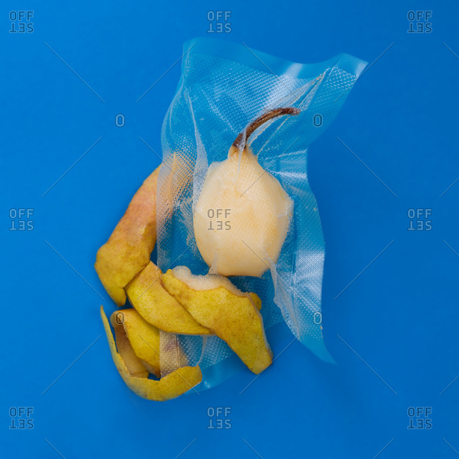 Top view of ripe yellow peeled pear in vacuum plastic bag and pear peel on blue background