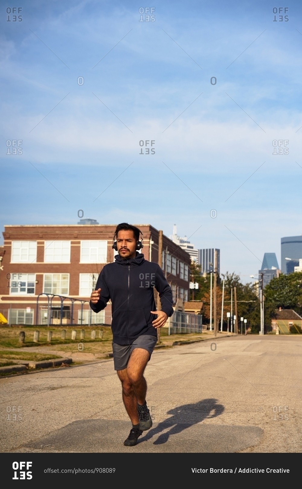 Concentrated Hispanic male athlete in sports wear with headphones running along empty road at downtown