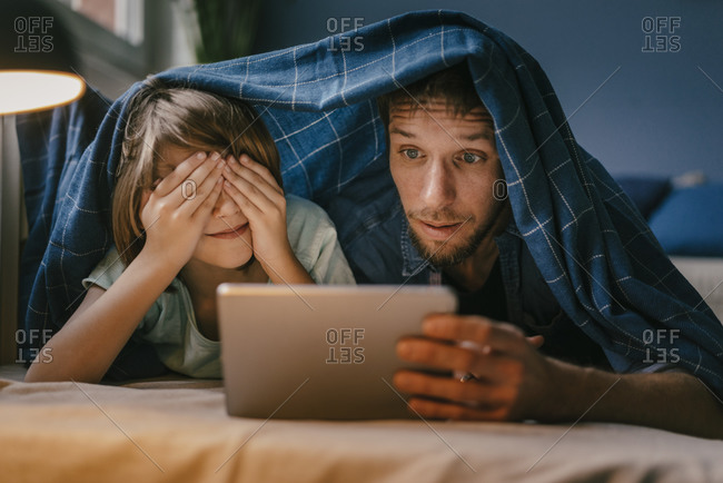 Excited father and son watching a movie on tablet under blanket