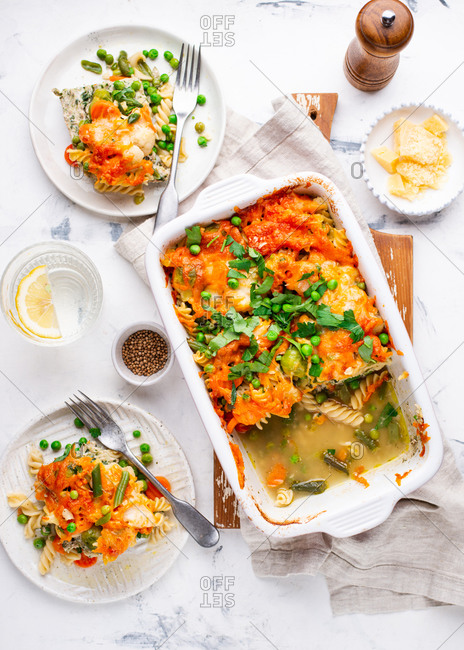 Baked macaroni and cheese casserole dish with vegetables and meat served on plates